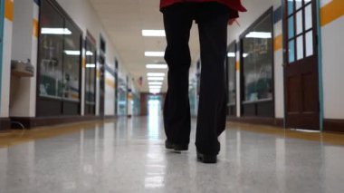 Okulda boş bir koridorda kameraya doğru yürüyen mutlu ve olgun bir kadın öğretmenin yavaş çekimde portresi..