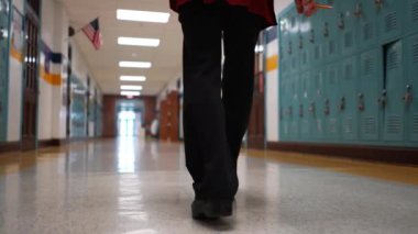 Okulda boş bir koridorda kameraya doğru yürüyen mutlu ve olgun bir kadın öğretmenin yavaş çekimde portresi..