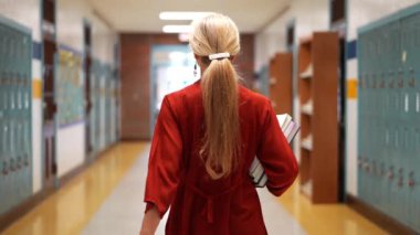 Okulda boş bir koridorda kameraya doğru yürüyen mutlu ve olgun bir kadın öğretmenin yavaş çekimde portresi..