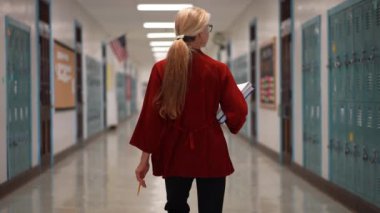 Okulda boş bir koridorda kameraya doğru yürüyen mutlu ve olgun bir kadın öğretmenin yavaş çekimde portresi..