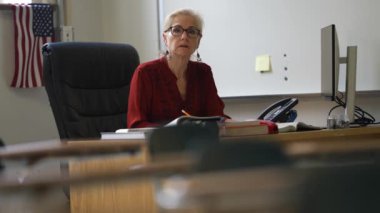 Sınıftaki gülümseyen kadın öğretmenin portresi yukarı bakar ve başparmağını kaldırır. Arka planda Amerikan bayrağı.