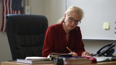 Sınıftaki gülümseyen kadın öğretmenin portresi yukarı bakar ve başparmağını kaldırır. Arka planda Amerikan bayrağı.