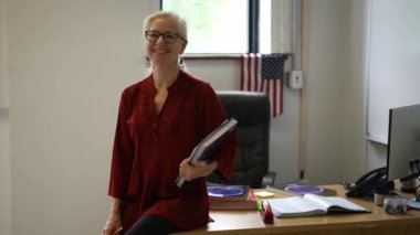 Sınıftaki gülümseyen kadın öğretmenin portresi yukarı bakar ve başparmağını kaldırır. Arka planda Amerikan bayrağı.