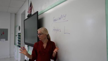 Boş bir sınıfta, interaktif bir beyaz tahta kullanarak geometri öğreten kadın öğretmenin geniş açı görünümü.