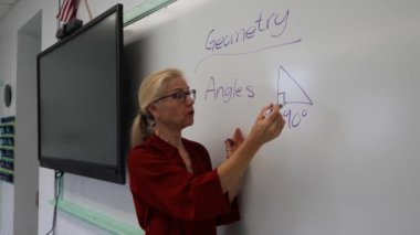Boş bir sınıfta, interaktif bir beyaz tahta kullanarak geometri öğreten kadın öğretmenin geniş açı görünümü.