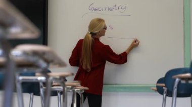 Boş bir sınıfta, interaktif bir beyaz tahta kullanarak geometri öğreten kadın öğretmenin geniş açı görünümü.