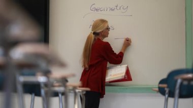 Boş bir sınıfta, interaktif bir beyaz tahta kullanarak geometri öğreten kadın öğretmenin geniş açı görünümü.