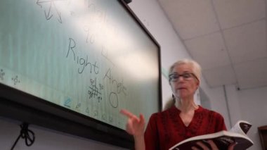 Boş bir sınıfta, interaktif bir beyaz tahta kullanarak geometri öğreten kadın öğretmenin geniş açı görünümü.