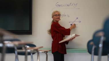 Boş bir sınıfta, interaktif bir beyaz tahta kullanarak geometri öğreten kadın öğretmenin geniş açı görünümü.