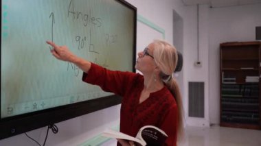 Boş bir sınıfta, interaktif bir beyaz tahta kullanarak geometri öğreten kadın öğretmenin geniş açı görünümü.