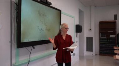 Boş bir sınıfta, interaktif bir beyaz tahta kullanarak geometri öğreten kadın öğretmenin geniş açı görünümü.