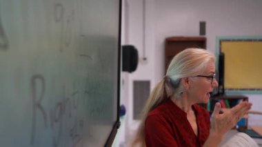 Boş bir sınıfta, interaktif bir beyaz tahta kullanarak geometri öğreten kadın öğretmenin geniş açı görünümü.