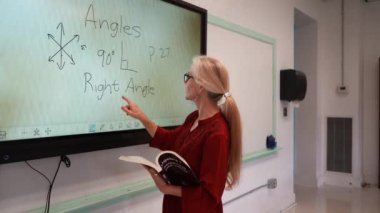 Boş bir sınıfta, interaktif bir beyaz tahta kullanarak geometri öğreten kadın öğretmenin geniş açı görünümü.