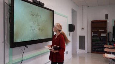 Boş bir sınıfta, interaktif bir beyaz tahta kullanarak geometri öğreten kadın öğretmenin geniş açı görünümü.
