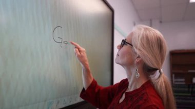 Boş bir sınıfta, interaktif bir beyaz tahta kullanarak geometri öğreten kadın öğretmenin geniş açı görünümü.