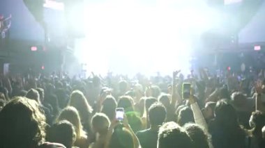 Seyirci kitlesinin geniş açılı görüntüsü, ellerinde telefonlar, ellerinde siluetleriyle bando sahnesinde, parlak mavi ışık saçan seyirciler. Festivaldeki mutlu insanlar müziğin tadını çıkarıyor