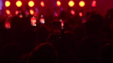 Seyircilerin yavaş çekim yakın çekimleri, ellerinde telefonlar, ellerinde siluetleriyle bando sahnesinde, parlak mavi, flaş ışıkta hareket eden seyirciler. Festivaldeki mutlu insanlar müziğin tadını çıkarıyor