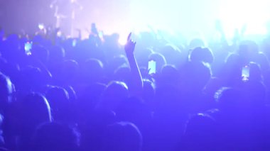 Seyirciler ellerini havaya kaldırmış, sahne arkasında parlak mavi ışık saçan hayranlar. Festivaldeki mutlu insanlar müziğin tadını çıkarıyor