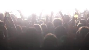 Seyirciler sahne ışıkları altında el sallayarak zıplıyorlar. Hayranlar hava siluetinde ellerini kaldırıyor, parlak mavi renkte hareket ediyor, flaş ışığı, sahne arkasında. Festivaldeki mutlu insanlar müziğin tadını çıkarıyor