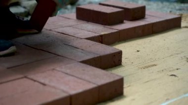 Avlu inşaatı için kumsala tuğla kaldırım döşeyen bir kadının yakın çekimi..