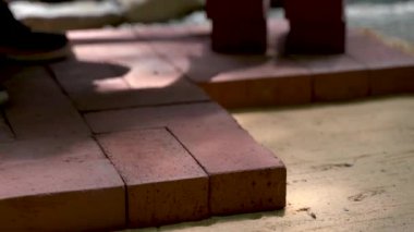 Avlu inşaatı için kumsala tuğla kaldırım döşeyen bir kadının yakın çekimi..