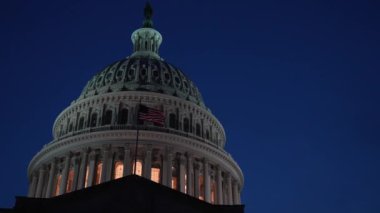 Gece Washington DC 'de bayrakları dalgalanan ve mimarisinde ışıklar olan ABD Capitol Kubbesi' nin merkezden sola yakın çekimleri. Boşluğu sola kopyala.