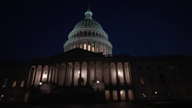 Gece Washington DC 'de bayrakları dalgalanan ve mimarisinde ışıklar olan Amerikan Kongre Binası' nın doğu yakasının yavaş çekim görüntüsü..