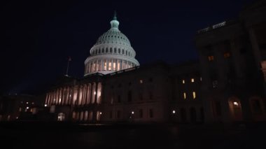 Geniş açı açısı solda. Gece Washington DC 'de mavi mor gökyüzüne karşı dalgalanan ışık ve bayraklarla Kongre Binası' nın doğu tarafını gösteriyor..