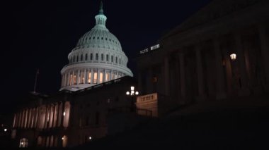 Gece Washington DC 'de mavi mor gökyüzüne karşı sallanan ışık ve bayraklarla ABD Kongre Binası' nı gösteren kamera sola hareket ediyor..