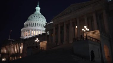 Gece Washington DC 'de mavi mor gökyüzüne karşı ışık ve bayraklar sallanan Amerikan Kongre Binası' nın doğu tarafını gösteren bir kamera sola hareket ediyor..