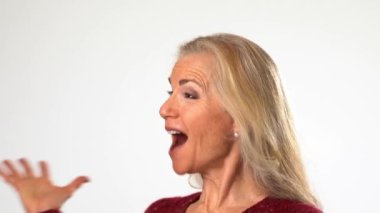 Heyecanlı, şaşırmış, gülümseyen olgun bir kadının yakın plan portresi. Beyaz arka plan stüdyosunda izole edilmiş sarı saçlarıyla kameraya bakan olgun bir kadın.