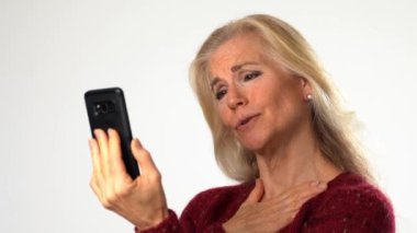 Sarışın, olgun bir kadın. Beyaz arka planda izole edilmiş akıllı telefon görüşmeleri yapıyor. Gülümseyen ve mutlu bir konsept olan arkadaş, aile işadamı.