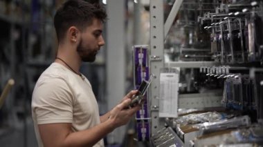 Sakallı bir adamın telefon kullanarak nalbur deposunda eşya aramasının yan görüntüsü.