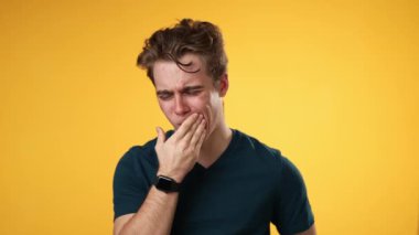 20 'li yaşlarda diş ağrısı sorunu olan genç hippi portresi stüdyoda sarı arka planda izole edilmiş.