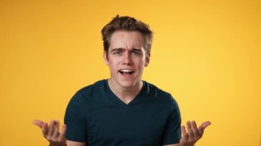 Hasta, yorgun, baş ağrısından bitkin düşmüş, 20 'li yaşlarda, sarı arka plan stüdyosunda yalnız poz veren genç adamın yavaş çekimleri. Ellerini başının üstüne koy.