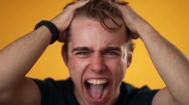 Sinirli, üzgün, hayal kırıklığına uğramış, 20 'li yaşlarda sarı arka planda izole edilmiş genç bir adamın yakın çekim yavaş portresi. Samimi duygular yaşam tarzı konsepti