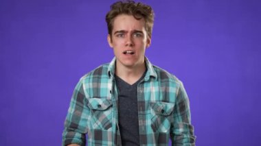 Kızgın ümitsizliğin portresi, mor arka planda izole edilmiş 20 'li yaşlardaki genç adamın yumrukları yüzünden üzgün..