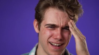 Mor arka plan stüdyosunda yalnız poz veren yorgun baş ağrısından bitkin düşmüş 20 'li yaşlardaki genç adam. Ellerini başının üstüne koy.