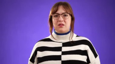 Kahverengi saçlı, gözlüklü, kazak giyen, başını sallayan üzgün genç bir kadın. Hayır, dur durak bilmeden hareket ediyordu. Mor arka planda, fotokopi alanı ile izole edilmişti..