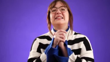 Dua ederken el ele tutuşup yalvarırken parmaklarını çapraz yap. Güzel esmer kadın portresi. 20 'li yaşlarda, mor arka plan stüdyosunda izole edilmiş..