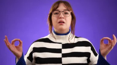 Esmer, uzun saçlı, 20 'li yaşlarda, kazaklı, ellerini yogaya koyan, meditasyon yapan, mor arka plandaki stüdyo resmine izole edilmiş bir şekilde sakinleşmeye çalışan genç bir kadın.