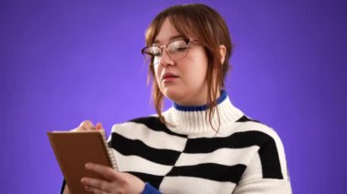 Düşünceli gazeteci kadın notlar alıyor, not defteri günlüğüne kalemle düşünceler yazıyor, liste yapmak için, iyi fikir. Güzel esmer kız öğrenci, mor stüdyo arka planında izole edilmiş.