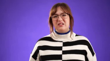 Gözlük takan ve 20 'li yaşlarda süveter giyen genç bir kadının portresi. Boyun ağrısı sorunu. Stüdyonun mor arka planında izole edilmiş.