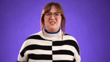 Hoşnutsuz, sinirli, üzgün, 20 'li yaşlardaki esmer kadın gözlük takıyor, kulaklarını kapatıyor mor arka plan stüdyo resminde izole edilmiş çığlıkları dinlemek istemiyor.