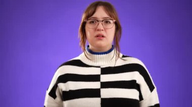 Kızgın sinirli genç kadın portresi, 20 'li yaşlarda, sessiz, gözlüklü, kazaklı ve mor arka planda izole edilmiş kaş kılı olan..