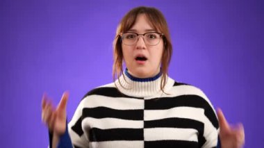 20 'li yaşlardaki güzel düşünceli genç bir kadının portresi, fotografla mor arkaplandaki fikirlerin patlamasını gösteren akıllara durgunluk veren jestler yapıyor..