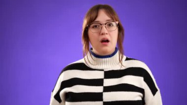 20 'li yaşlardaki güzel düşünceli genç bir kadının portresi, fotografla mor arkaplandaki fikirlerin patlamasını gösteren akıllara durgunluk veren jestler yapıyor..