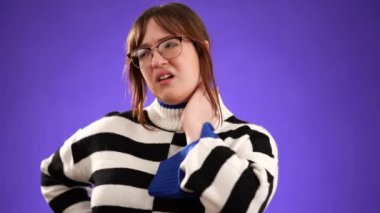 20 'li yaşlarda, boynu ağrıyan omuz ağrısı olan genç bir kadının portresi stüdyoda mor arka planda izole edilmiş.