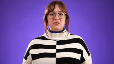 Mutlu, güzel bir kadının portresi 20 'li yaşlarda omuz silkiyor ve mor arka planda izole edilmiş bir şekilde el kol hareketi yapıyor..