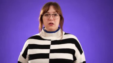 Korkmuş esmer kadın 20 'li yaşlarda mor arka plan stüdyosunda yalnız poz veriyor. İnsanların yaşam tarzı konsepti. Ağız kaplayan gözler ve saklanan eller.